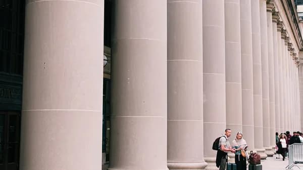 People walking past large stone columns outdoors