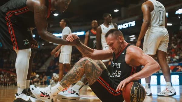A basketball player helps his teammate up from the floor.
