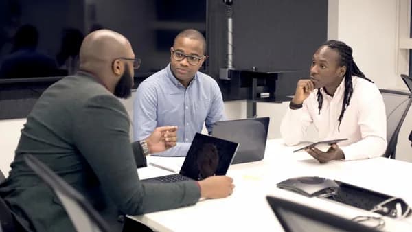 a group of people sitting around a table with laptops