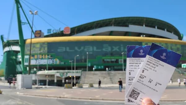 A person holding up two tickets in front of a stadium