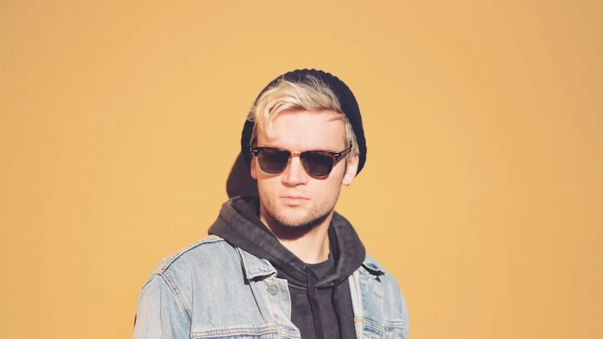 standing man in black framed sunglasses, black beanie cap and blue denim jacket