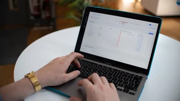 Hands typing on a laptop with a spreadsheet on screen.