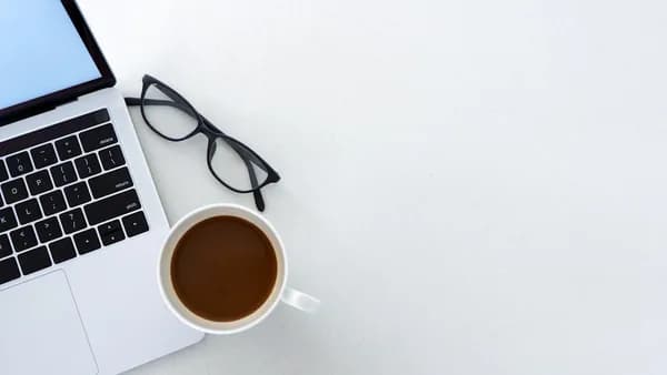 Laptop, coffee, and glasses on a white desk.