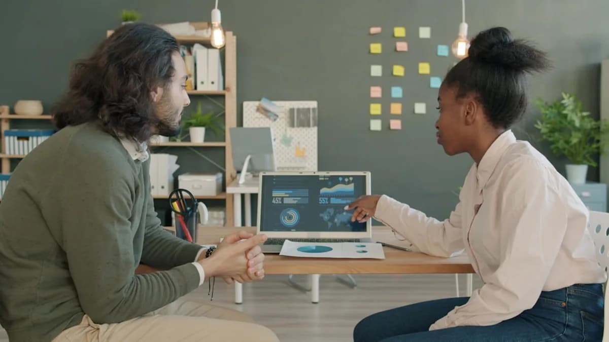 Two colleagues discussing data on a laptop screen.