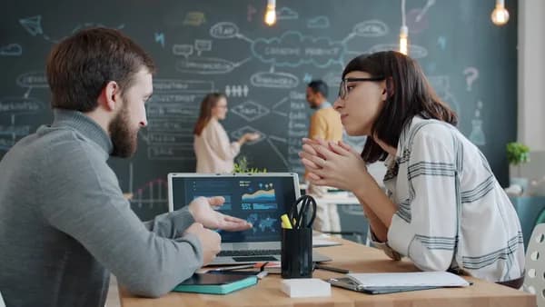 Two colleagues discussing charts on a laptop screen.