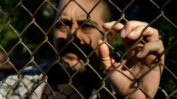 a man behind a chain link fence making a face