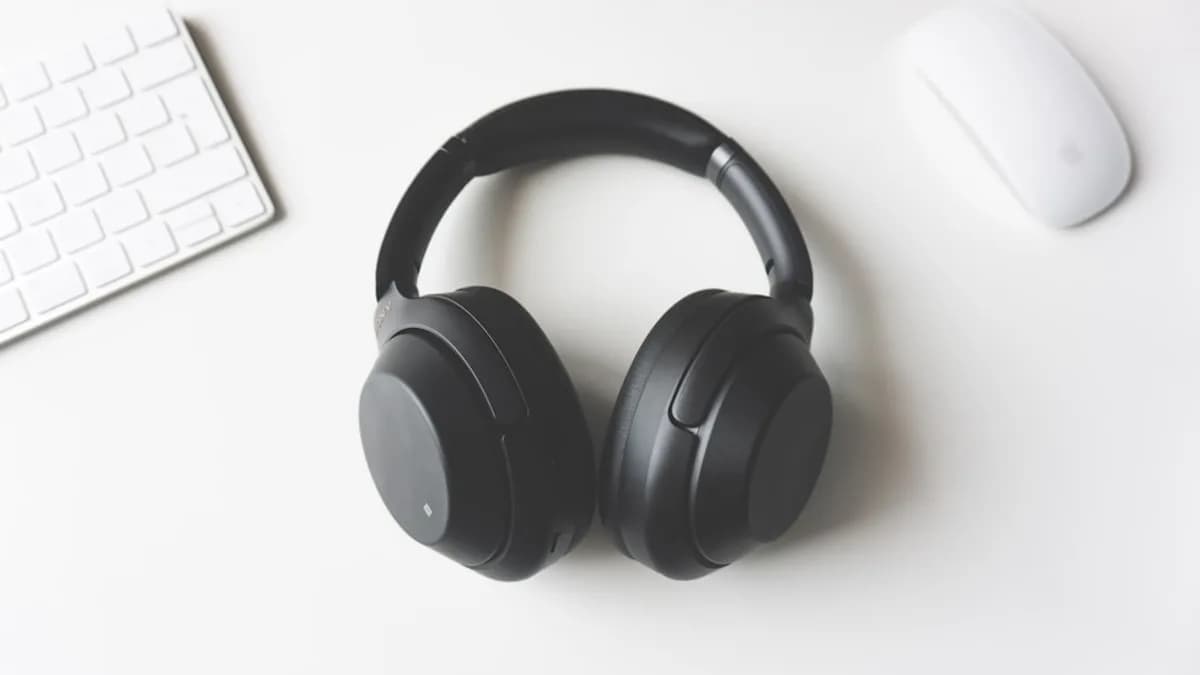black wireless headphones between Apple Keyboard and Apple Magic Mouse on white surface