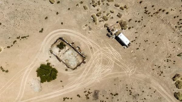 Aerial view of a derelict structure and vehicle in desert.