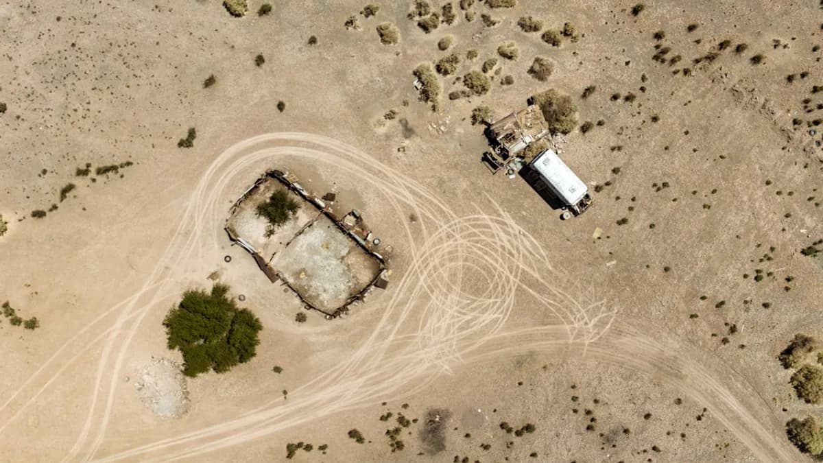 Aerial view of a derelict structure and vehicle in desert.